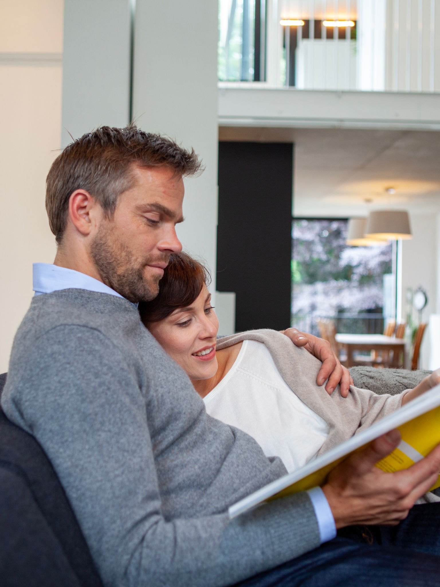 Koppel knuffelt en ontspant op hun bank terwijl ze een boek lezen bij een perfecte temperatuur