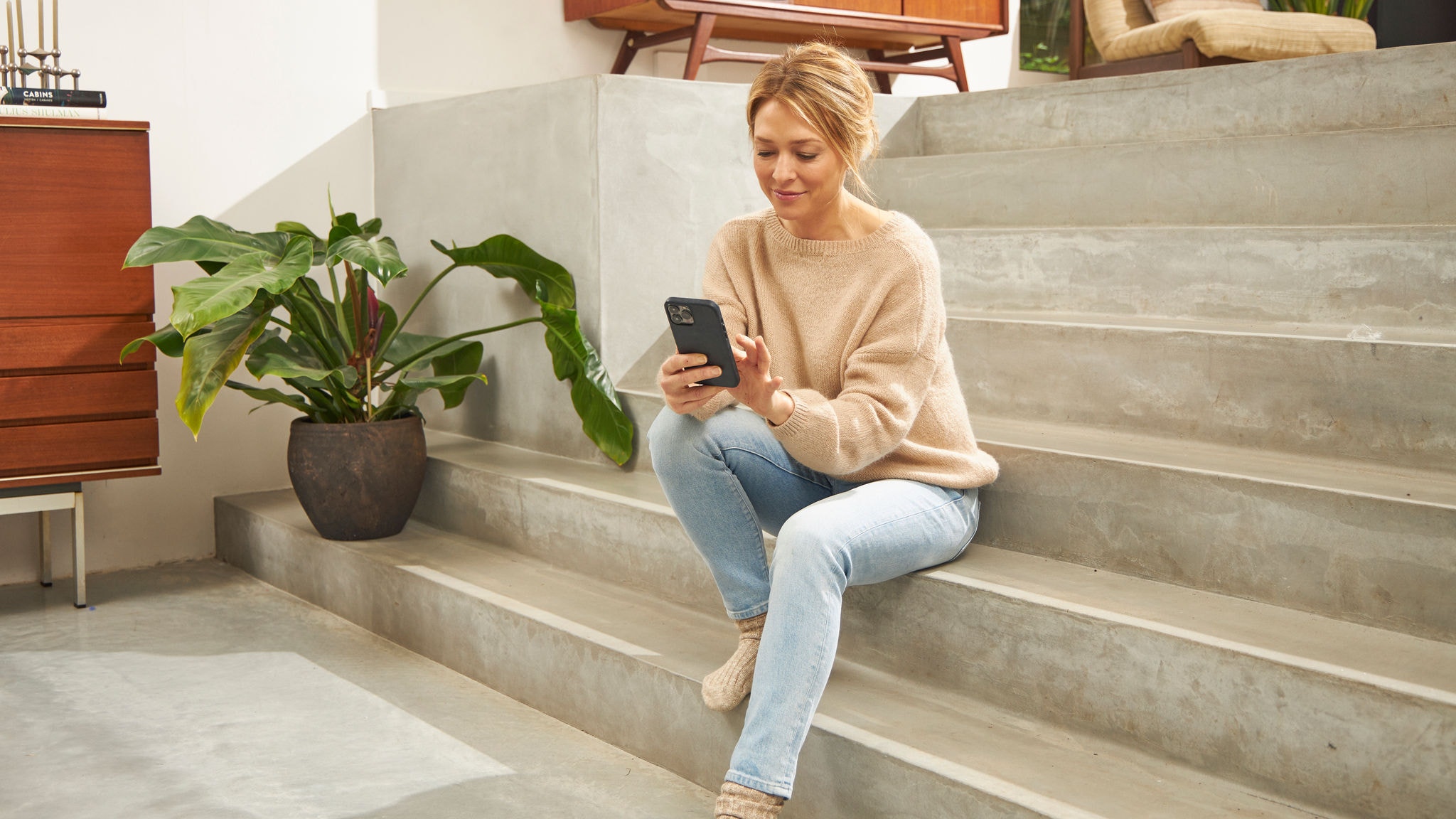 Femme assise dans les escaliers de son logement, utilisant l'application Onect sur son téléphone portable