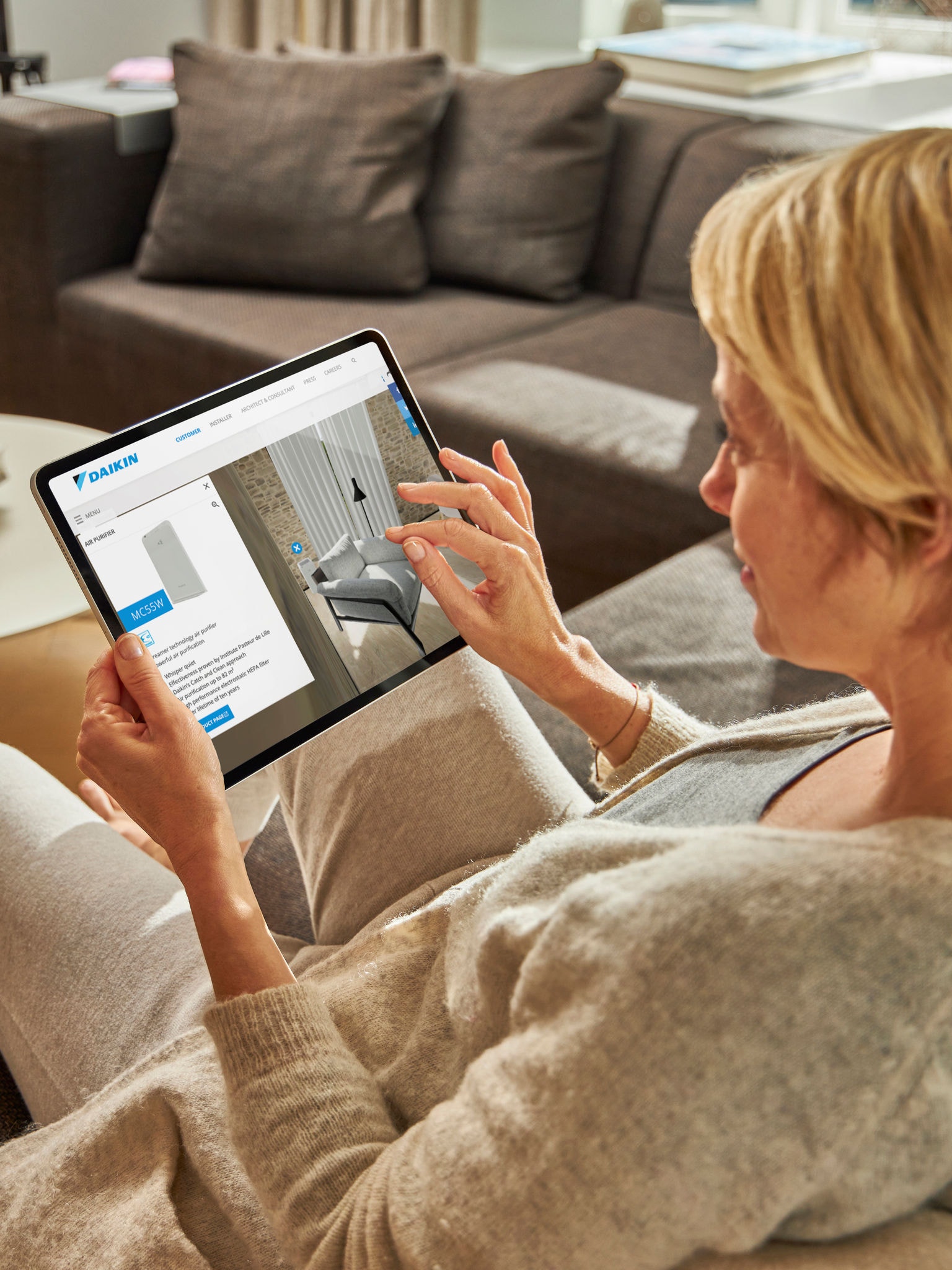 Vrouw zit op een zetel en bekijkt lucht/water-warmtepompen in het virtuele ervaringscentrum op haar tablet