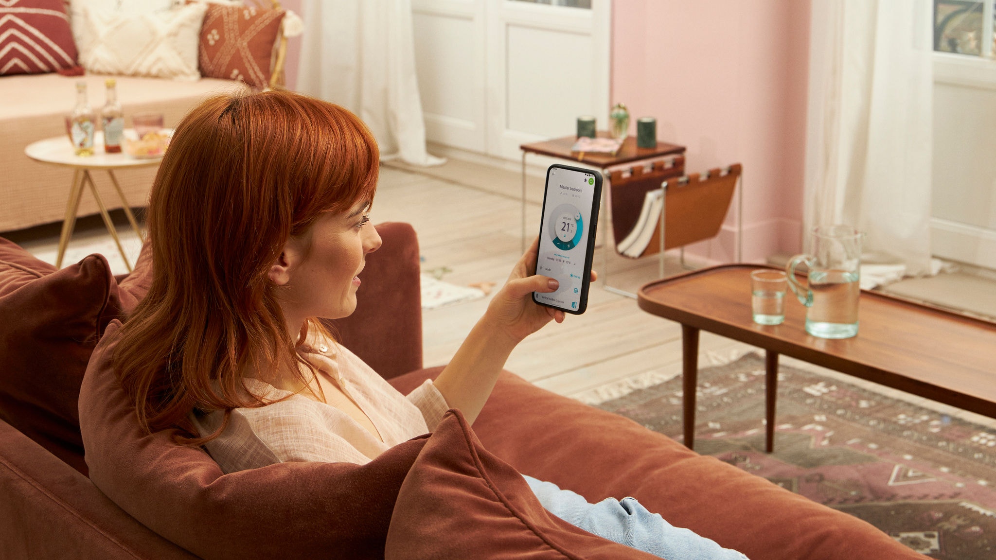 Vrouw zit in zetel thuis en controleert de Onecta-app op haar mobiele telefoon