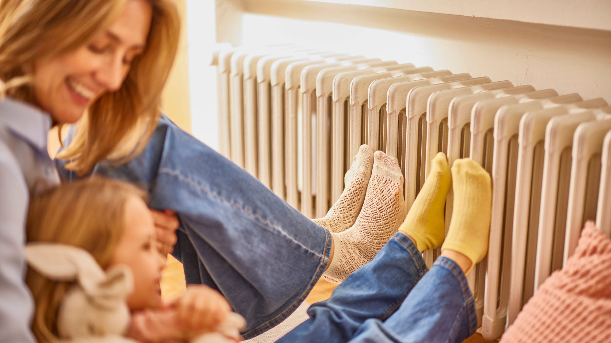 Moeder en dochter warmen hun voeten aan een radiator in een warme en aangename woning