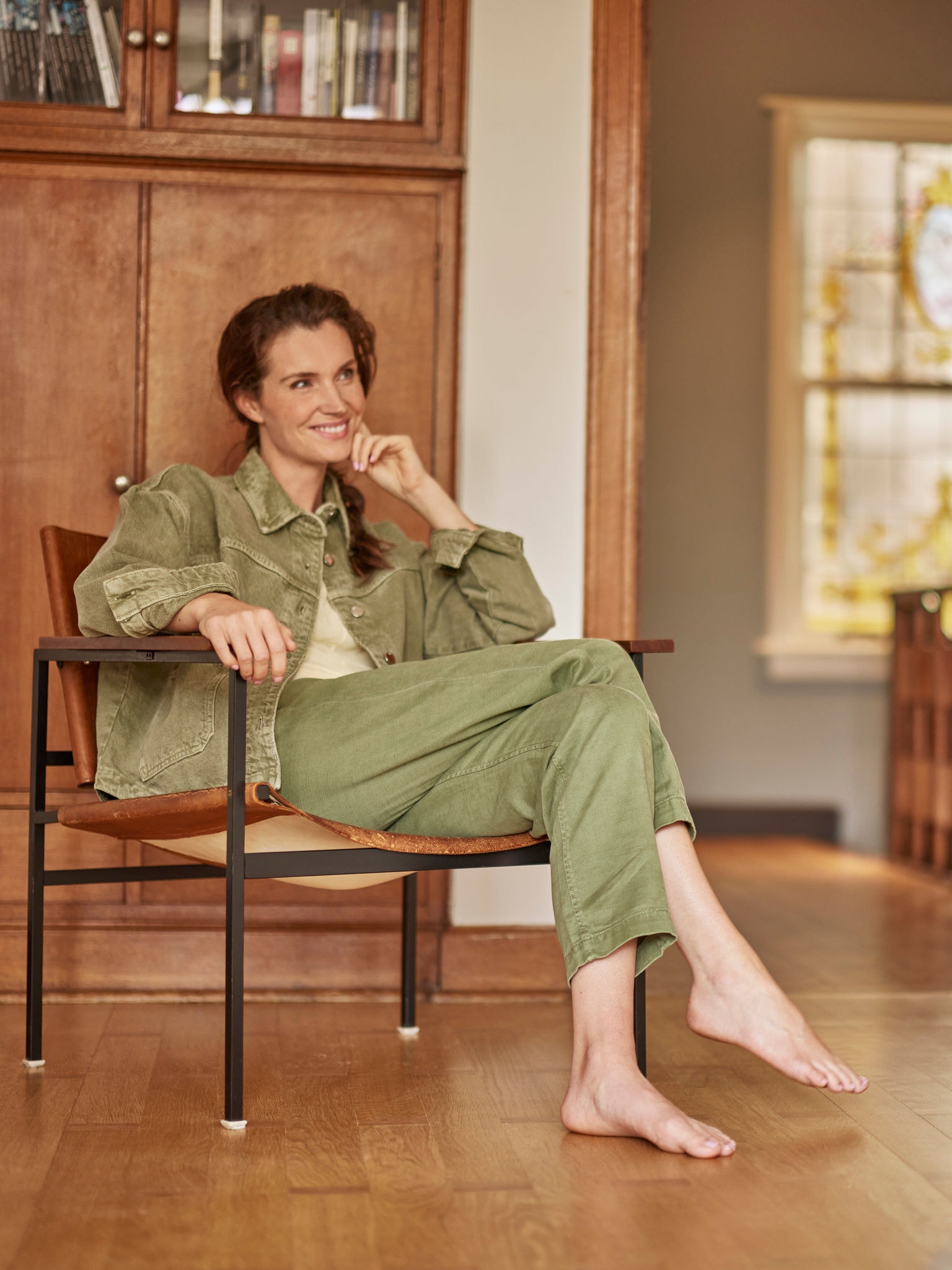 Femme assise dans son fauteuil, pieds nus, souriante et regardant devant elle