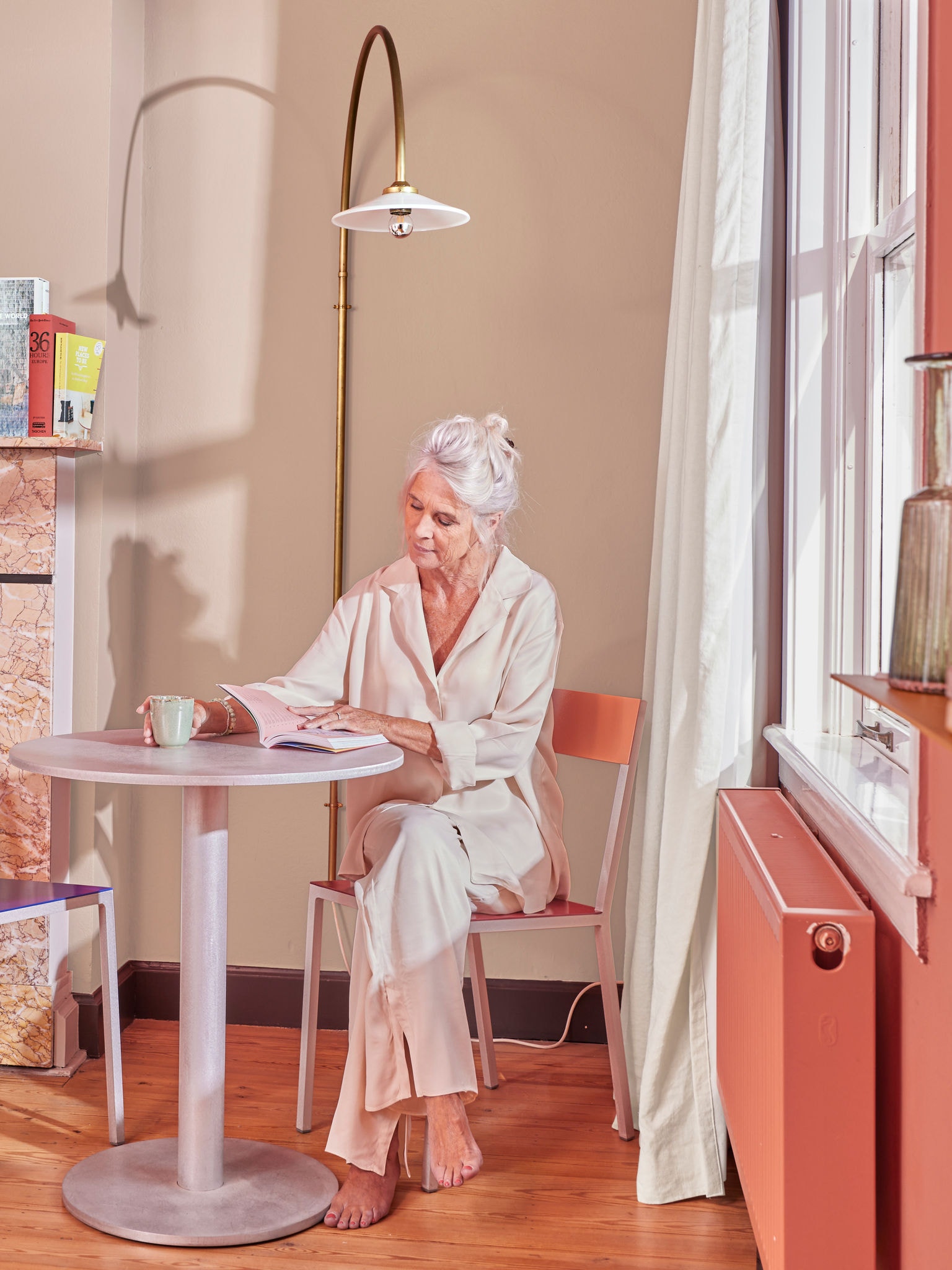 Vrouw die aan een tafel bij de radiator zit te lezen, met een verwarming via een warmtepomp