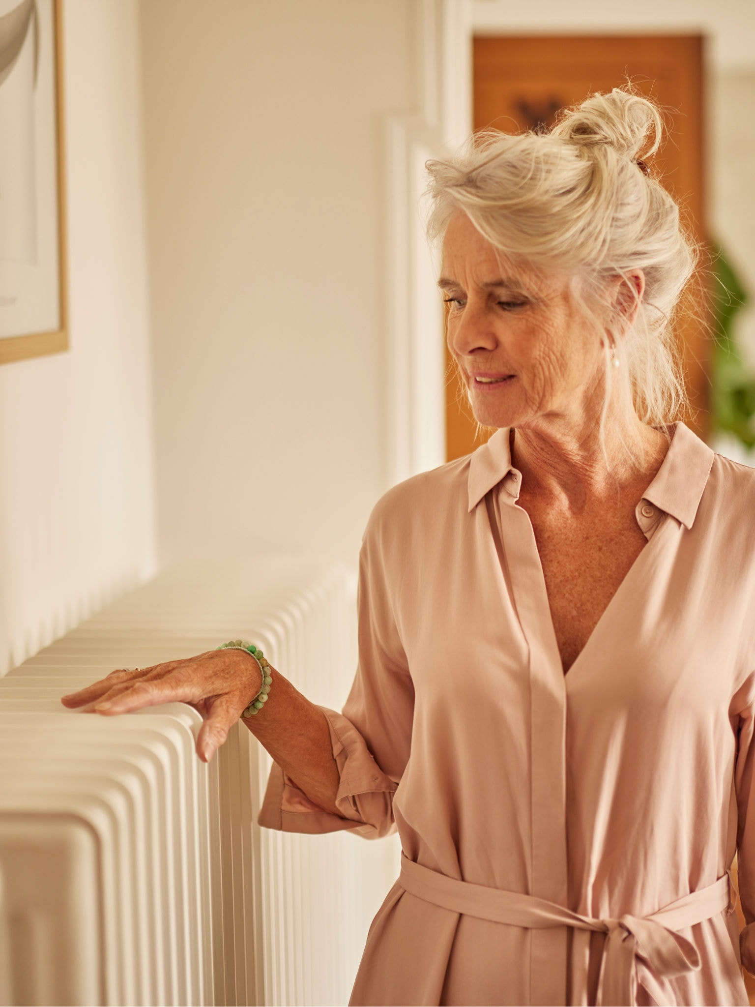 Vrouw die haar handen warmt aan een radiator, in combinatie met een luchtwarmtepomp in de slaapkamer