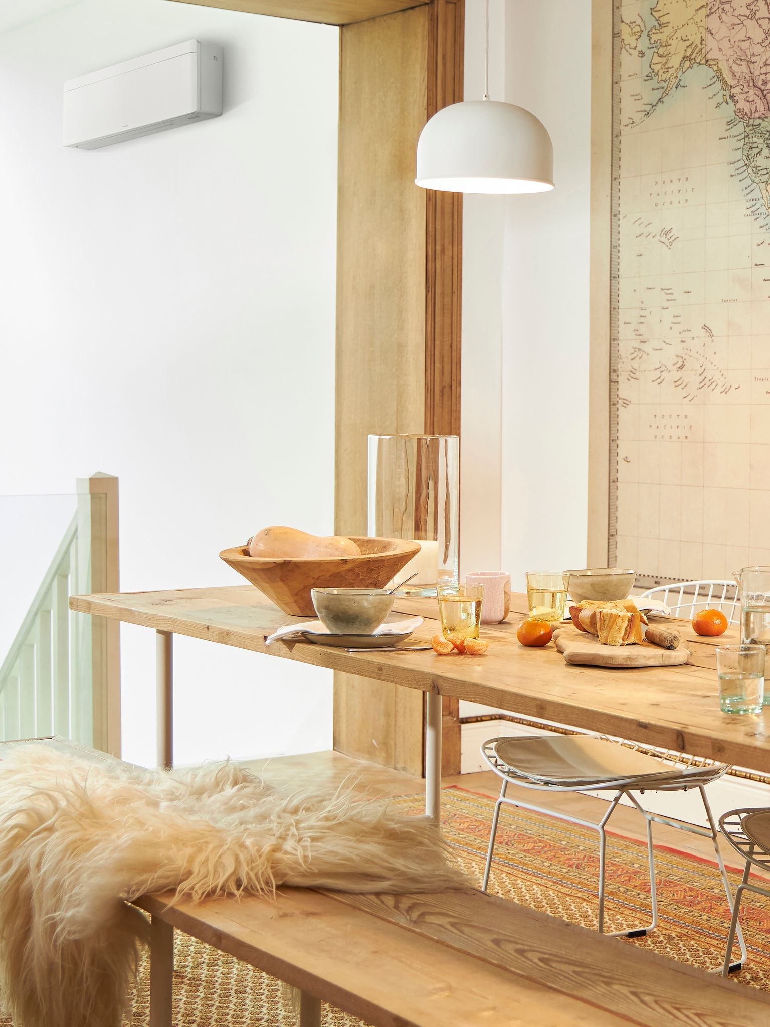 Table dressée avec de la nourriture et des fruits pour le déjeuner dans une pièce lumineuse, où l'on voit un climatiseur près de l’escalier.