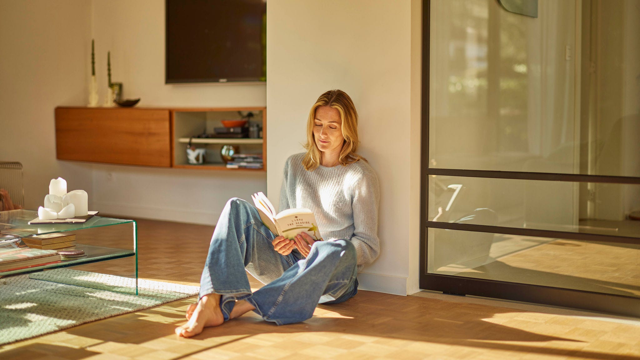 Femme en train de lire, assise sur un parquet et profitant d’une pièce parfaitement chauffée grâce au chauffage par le sol