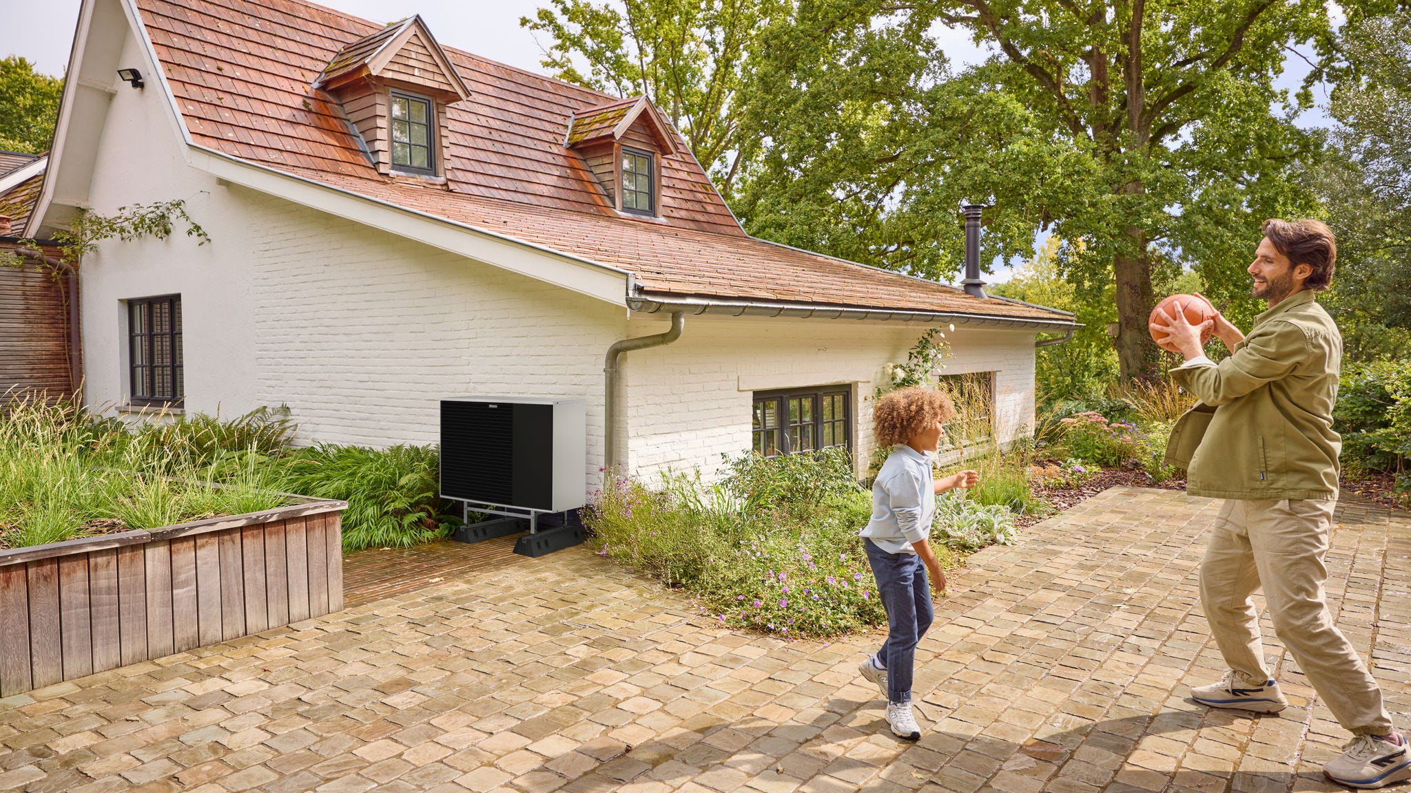 Père jouant avec son enfant dans un jardin, à proximité d’une pompe à chaleur