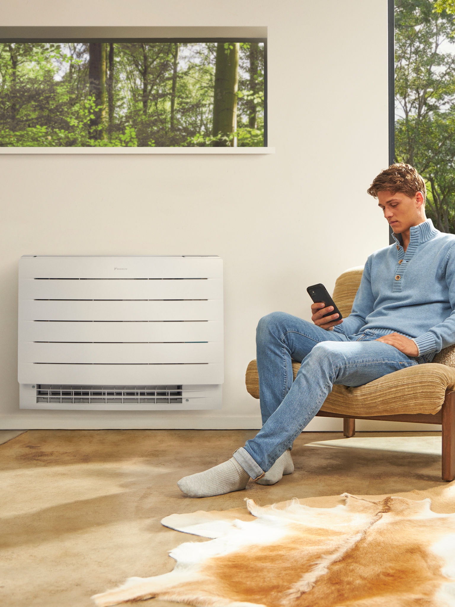 Homme assis dans une pièce claire en train de regarder son téléphone, avec une pompe à chaleur sur le mur derrière lui