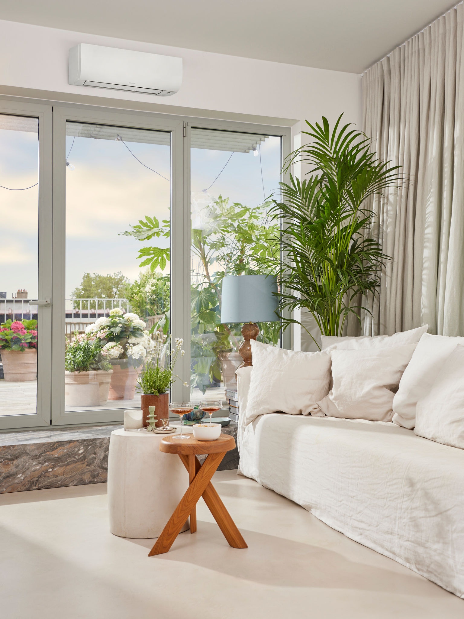 Salon lumineux et confortable où l’apéritif est servi, avec de grandes portes vitrées menant à une terrasse et au-dessus desquelles se trouve un climatiseur.