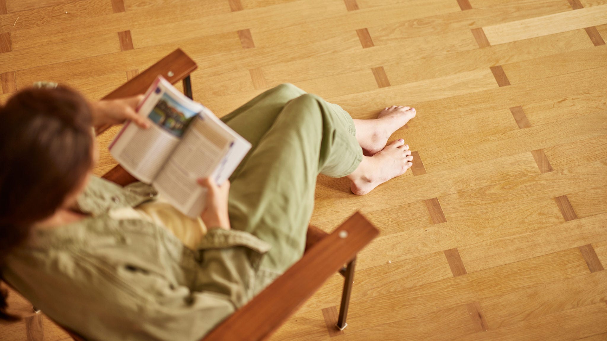 Femme assise sur un parquet, pieds nus, profitant du confort du chauffage par le sol tout en lisant un livre