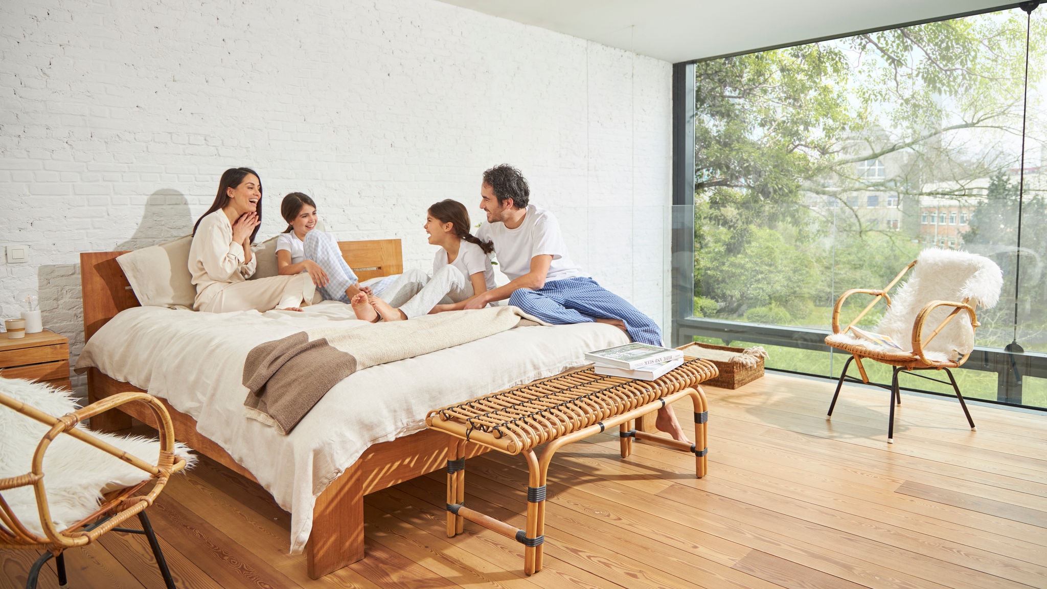 Een gezin in gesprek op een bed in een slaapkamer met een grote glazen wand, een goede binnenluchtkwaliteit en veel natuurlijk licht