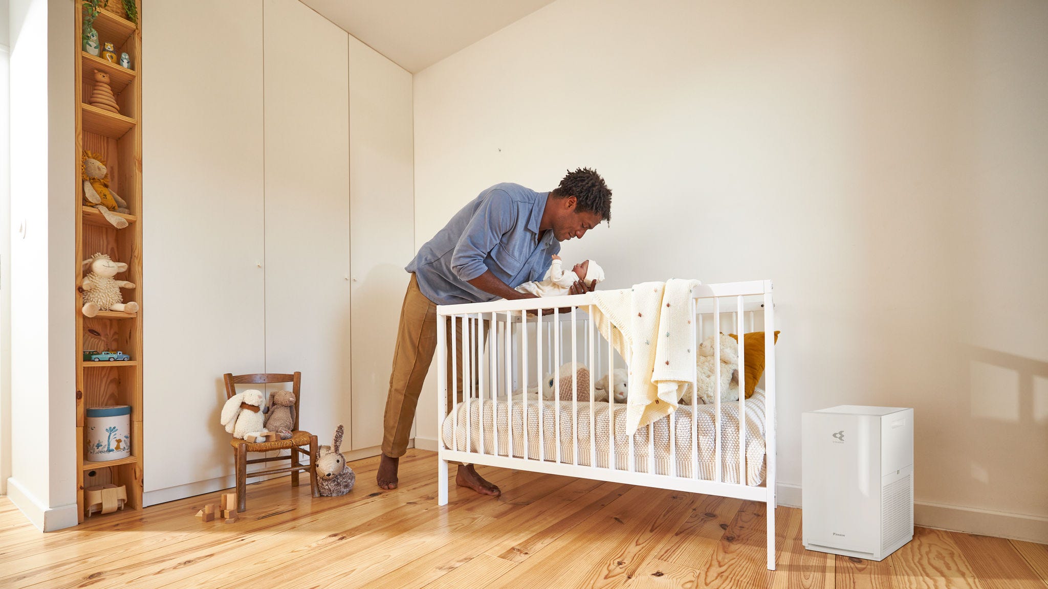 Vader die zijn baby instopt in een rustige babykamer met een luchtreiniger in de buurt