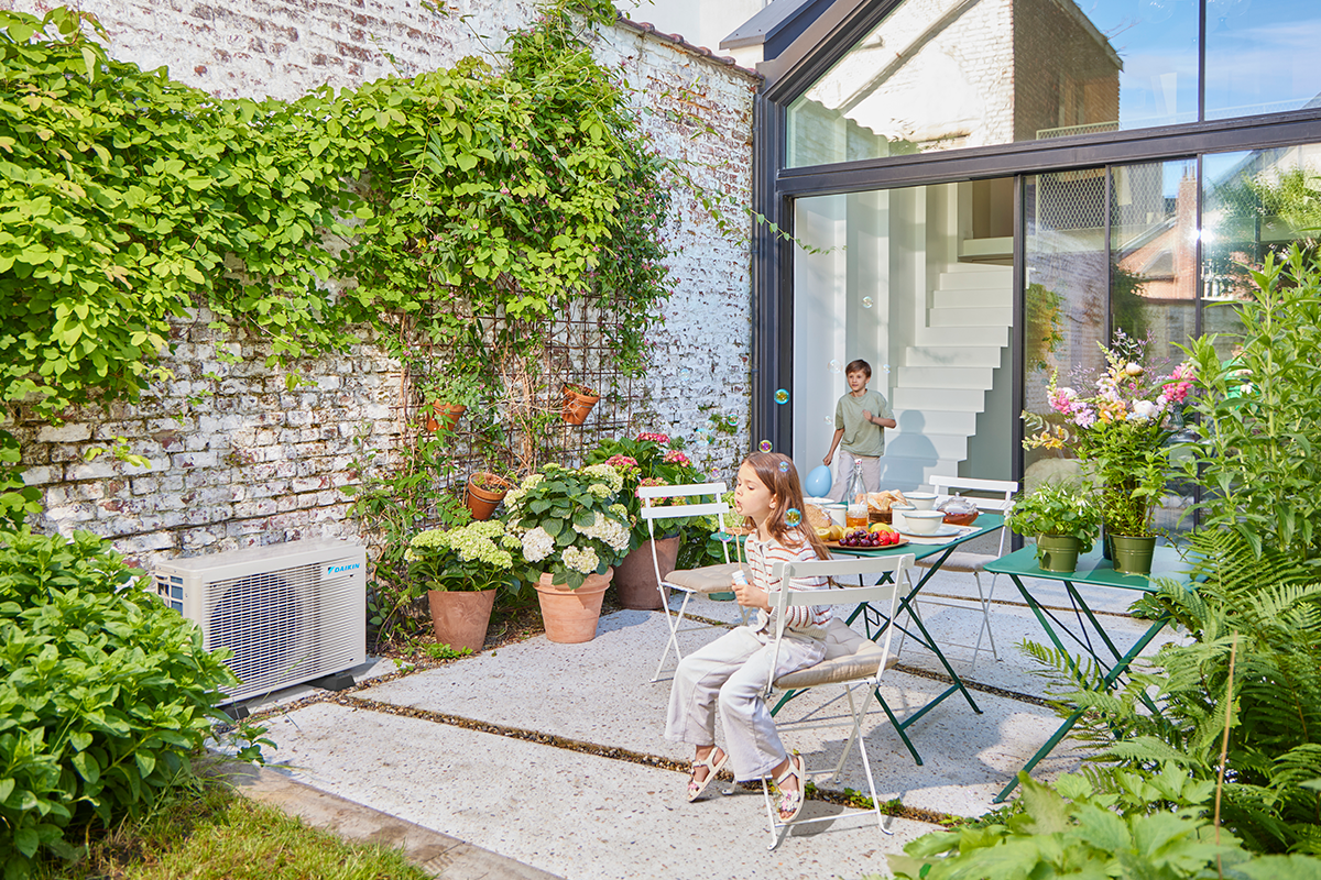 Enfants jouant aux billes sur une terrasse de jardin à proximité d'une pompe à chaleur extérieure