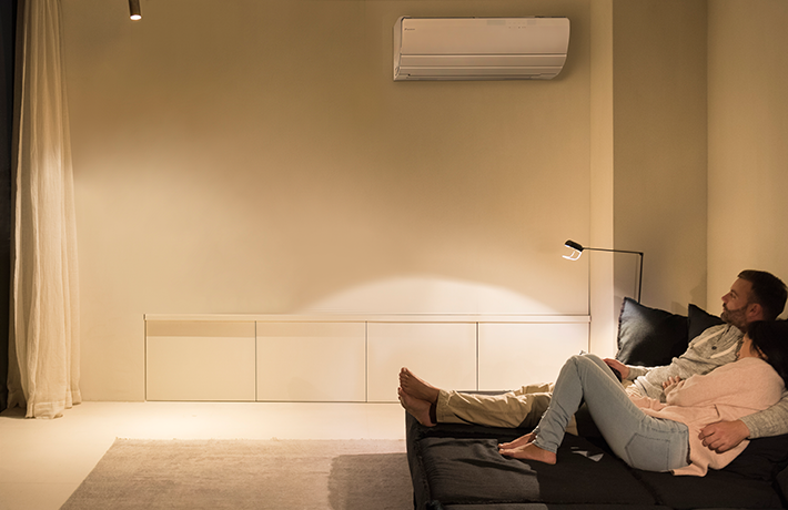 Stel op een sofa naast een aan de muur gemonteerde Daikin ururu sarara.